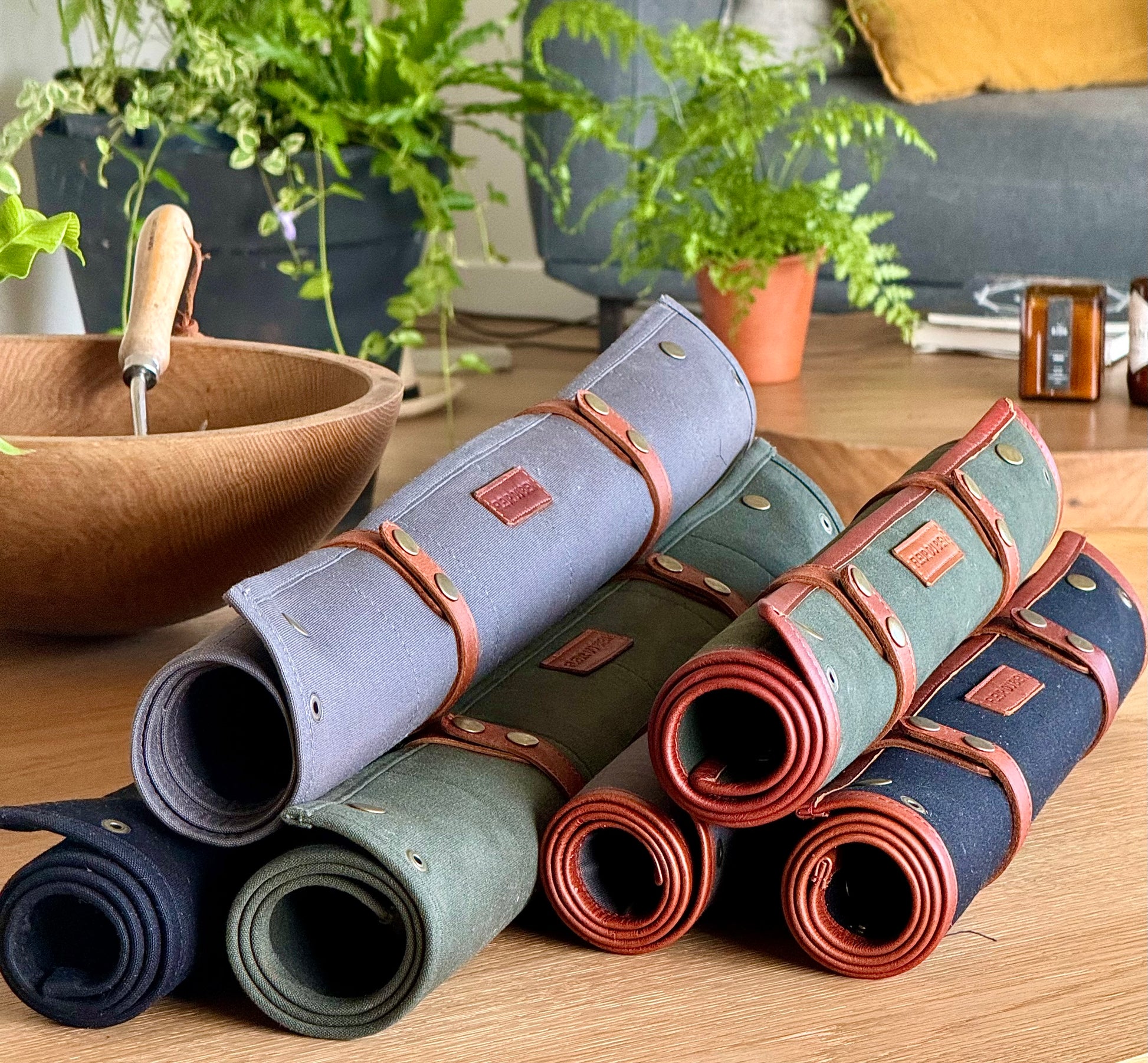 rFleur Du Bien indoor repotting mats in all colors – 30x20 and 30x30 inches with leather trims, in gray, black, and green. Displayed on an oak designer table in a luxury apartment. Perfect to match the Fleur Du Bien garden tool set and apron. Ideal for indoor gardening, herb potting, transplanting, and DIY projects with no mess, combining elegance, durability, and eco-friendly design