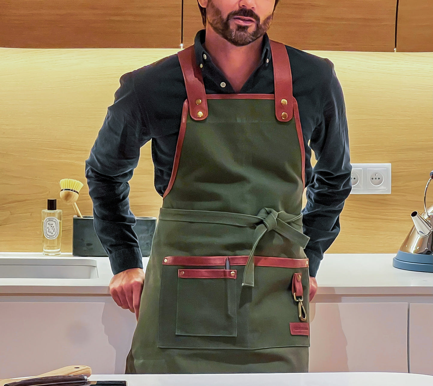 Fleur Du Bien eco-friendly apron styled in minimalist French kitchen setting. Fleur Du Bien eco-friendly apron worn by a man in the kitchen, also for barbecuing, gardening, and landscaping outdoors, showcasing adjustable straps and multiple pockets