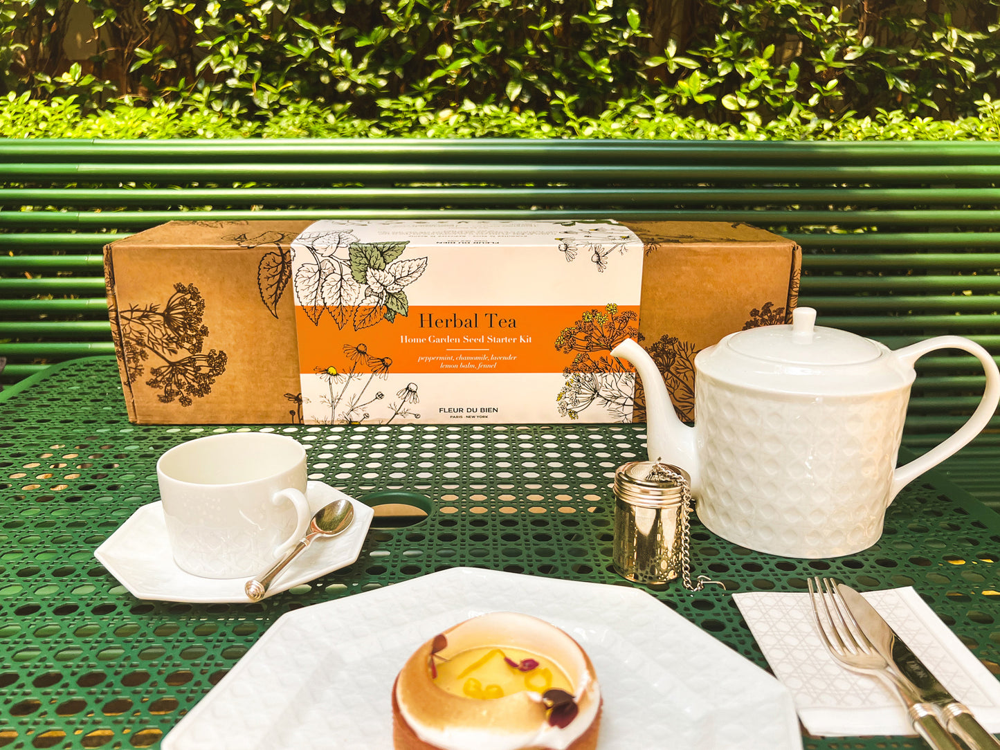 Fleur Du Bien Loose Leaf Green Tea & Herb Garden Kit box with stainless steel strainer and lemon cake, styled on luxurious Dior-inspired Parisian table setting